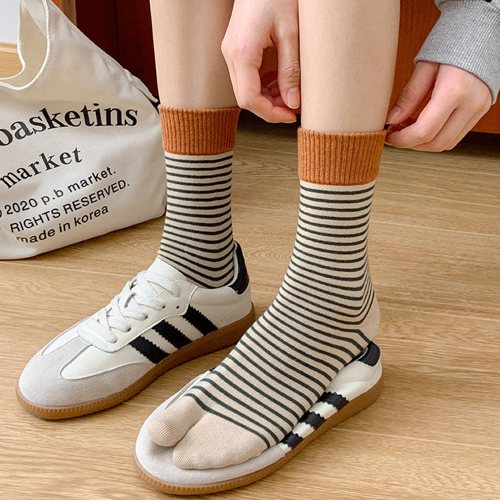 Person wearing striped socks with orange tops, standing on a wooden floor next to a white bag.