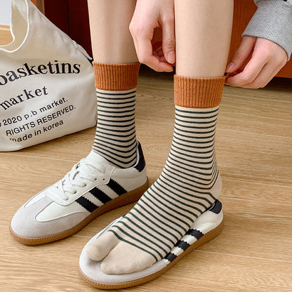Person wearing striped socks with orange tops, standing on a wooden floor next to a white bag.