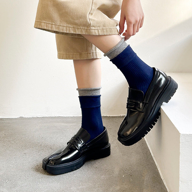 Person wearing black shoes and blue socks on a neutral background
