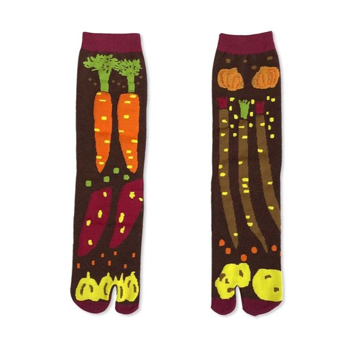 A pair of Japanese tabi socks with a colorful vegetable pattern, including carrots and pumpkins, on a brown background.