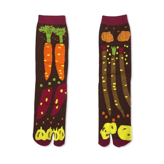 A pair of Japanese tabi socks with a colorful vegetable pattern, including carrots and pumpkins, on a brown background.